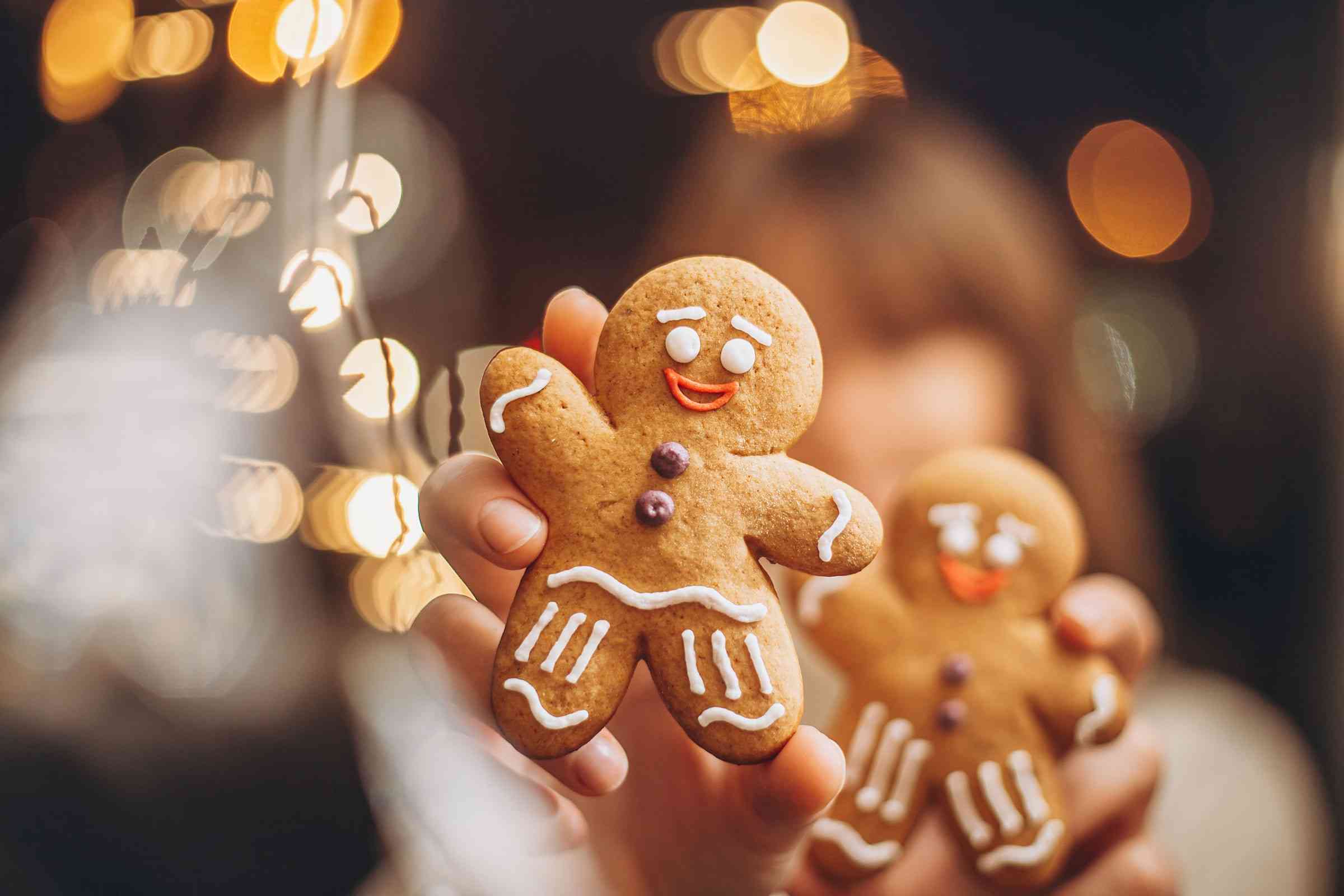 Hände halten zwei Lebkuchenmänner vor weihnachtlichen Lichtern